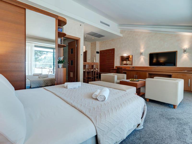 Habitación de hotel luminosa con cama grande, muebles blancos y TV moderna en la pared.