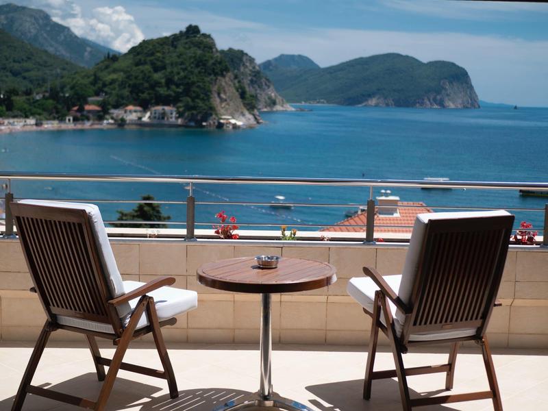 Vista al mar desde un balcón con dos sillas de madera y una mesa pequeña.