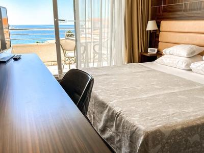 Modernes Hotelzimmer mit Bett, Schreibtisch und Blick auf den Balkon mit Meerblick.
