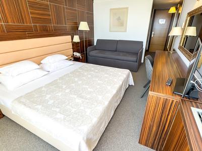 Modernes Hotelzimmer mit Doppelbett, Sofa, Schreibtisch und Holzmöbeln in warmen Tönen