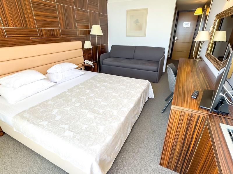 Modernes Hotelzimmer mit Doppelbett, Sofa, Schreibtisch und Holzmöbeln in warmen Tönen