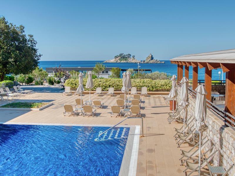Hotelpool mit Liegestühlen und Blick auf das Meer und die Felsen im Hintergrund
