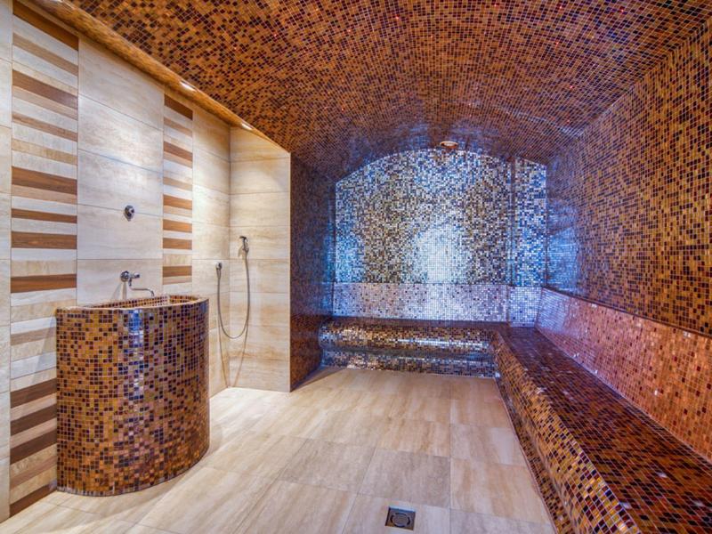 Moderner Spa-Raum mit Mosaikfliesen, Sauna-Bänken und einer Dusche an der Wand.