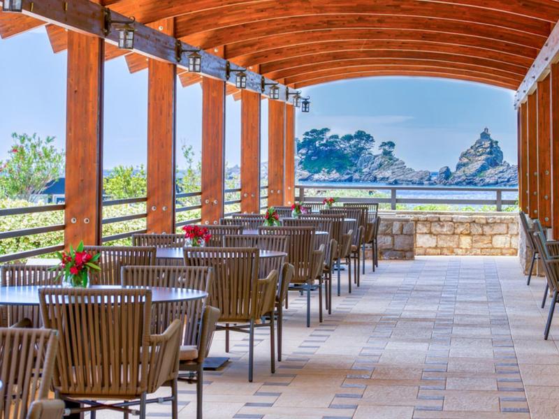Überdachte Terrasse mit Holzbalken und Stühlen neben Tischen in einem Hotel.