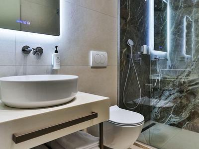 Moderne Hoteldusche mit Marmorwänden, Glasabtrennung, Waschbecken und WC in hellem Badezimmer.