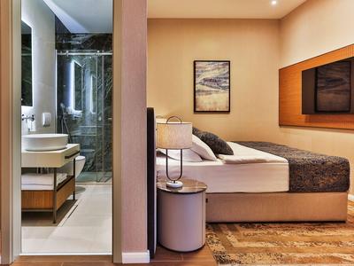 Modern eingerichtetes Hotelzimmer mit Bett, Fernseher und angrenzendem Bad mit Glasdusche.