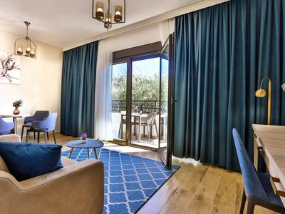 Gemütliches Hotelzimmer mit Wohnbereich und Balkon, großen blauen Vorhängen und Holzboden.