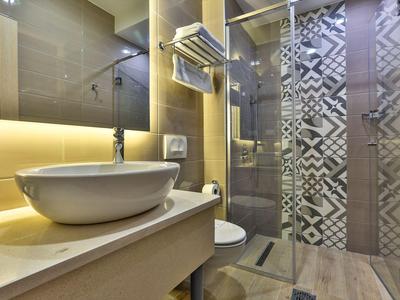 Modernes Badezimmer mit rundem Waschbecken, beleuchtetem Spiegel und gemusterter Duschwand.