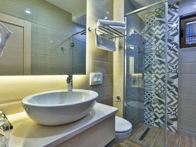 Modernes Badezimmer mit beleuchtetem Spiegel, Waschbecken auf der Theke und Duschkabine mit Musterfliesen.