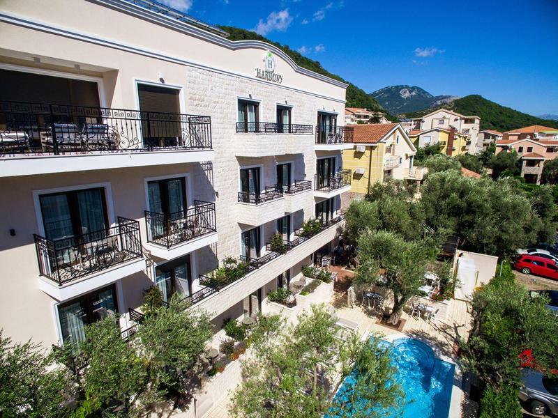 Mehrstöckiges Hotel mit Balkonen, grünem Garten und kleinem blauen Pool unter blauem Himmel.