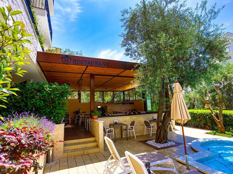 Außenbereich mit Swimmingpool, Sitzgelegenheiten, Sonnenschirm und grünem Garten unter blauem Himmel.