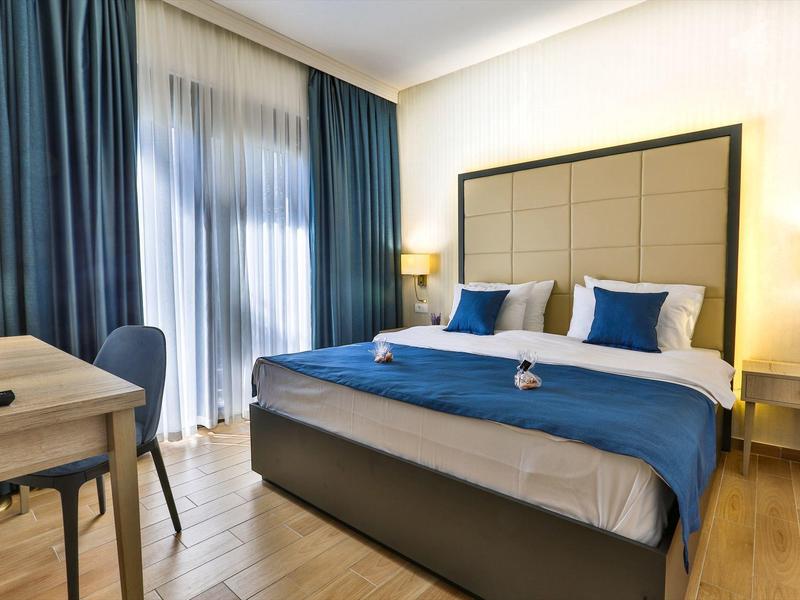 Helles Schlafzimmer mit großem Bett, blauen Vorhängen und Holzboden, moderne Beleuchtung.