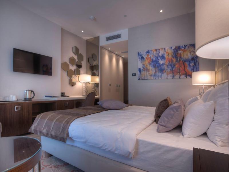 Modernes Hotelzimmer mit großem Bett, farbigem Wandbild und Holz-Möbeln in warmem Licht.