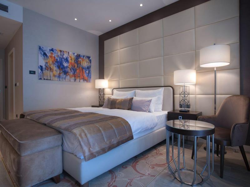 Modernes Schlafzimmer mit großem Bett, gepolstertem Kopfteil, zwei Nachttischen und abstraktem Bild.