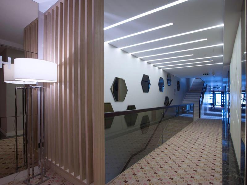 Moderner Flur mit geometrischen Wanddekorationen, Glasbrüstung und linearen Deckenlichtern.