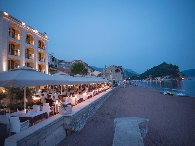 Abendliche Strandpromenade mit beleuchtetem Restaurant und ruhigem Meer im Hintergrund.