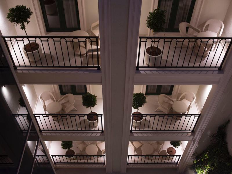 Innenhof mit vier gleichmäßigen, beleuchteten Balkonen, Pflanzen und Sitzmöbeln, perspektivisch von unten.