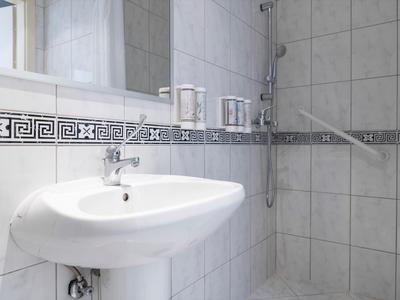 Helles Badezimmer mit weißem Waschbecken und Walk-in-Dusche mit Glaswand und Duschkopf.