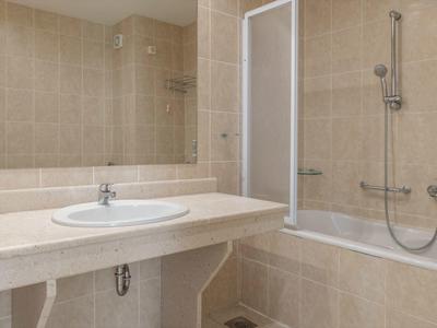 Modernes Badezimmer mit hellen Fliesen, einem Waschbecken und einer Badewanne mit Duschvorhang.