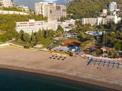 Strand mit Liegestühlen vor Hotels und bewaldeten Hügeln bei Sonnenlicht.