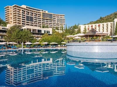 Großes Hotel vor blauem Himmel mit Pool und Sonnenschirmen im Vordergrund.