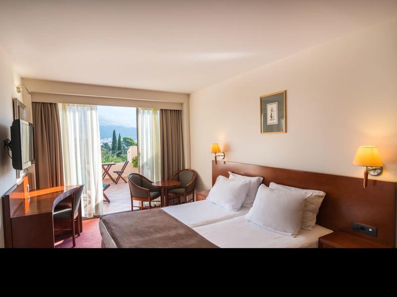 Hell eingerichtetes Hotelzimmer mit Doppelbett, Schreibtisch und Balkon mit Sitzgelegenheit