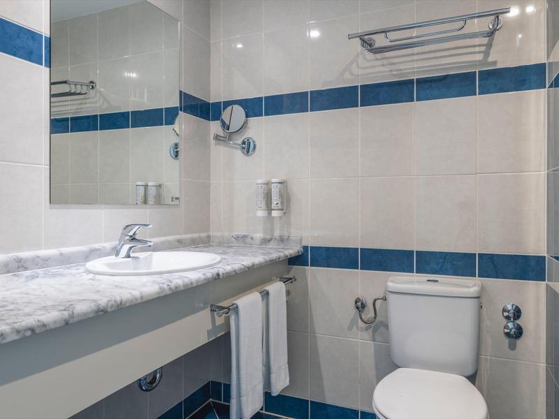 Kompaktes Badezimmer mit Waschbecken, großer Spiegel und Toilette, weiße und blaue Fliesen.