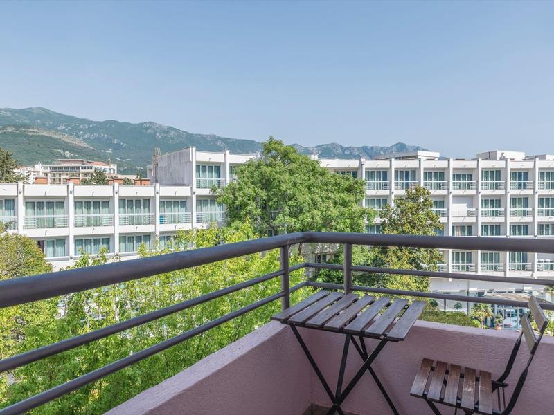 Balkon mit kleinem Tisch und Stühlen mit Blick auf moderne Gebäude und Berge im Hintergrund.