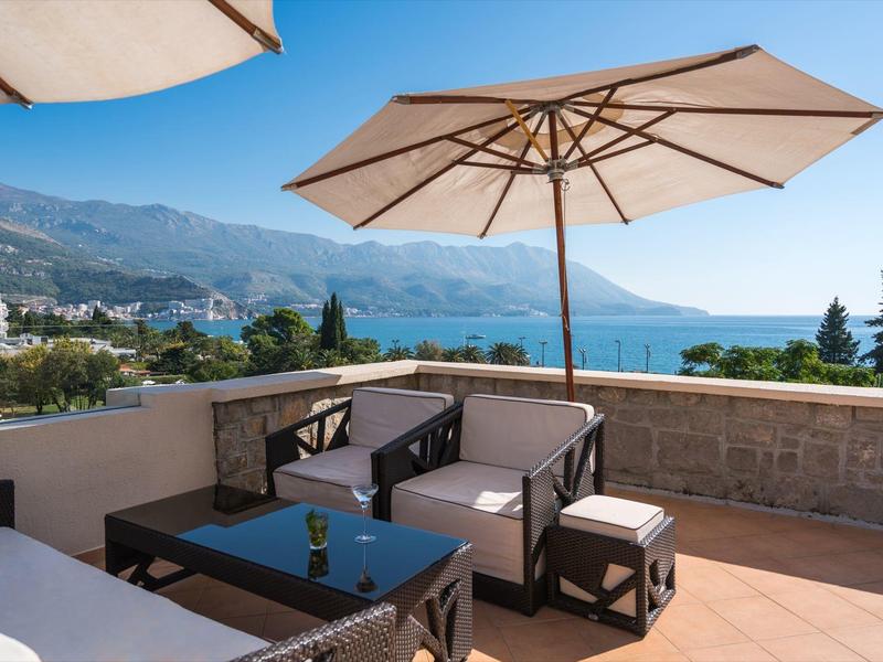 Terrasse mit Sitzmöbeln und Sonnenschirm mit Blick auf das Meer und Berge bei klarem Himmel