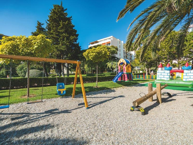 Kinderspielplatz mit Schaukel, Rutsche und Klettergerüst in einem Park mit Palmen