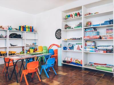 Kinderspielzimmer mit bunten Stühlen, Tischen und Regalen voller Spielzeug und Gesellschaftsspiele.