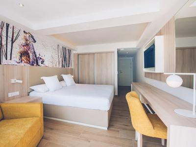 Jasny pokój hotelowy z dwoma łóżkami, drewnianymi meblami, żółtymi krzesłami i nowoczesnym wystrojem.