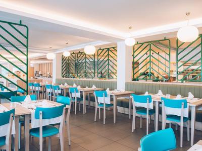 Jasne wnętrze restauracji z turkusowymi krzesłami i białymi stołami nakrytymi do posiłków.