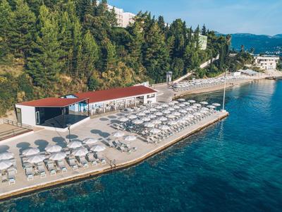 Nadmorska promenada z leżakami i parasolami obok czystej wody i zalesionego wzgórza.