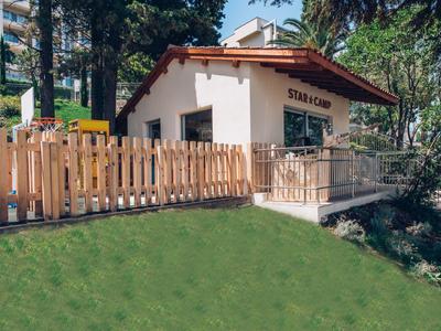 Kleines weißes Gebäude mit rotem Dach und Holzzaun, umgeben von Grünflächen und Bäumen.