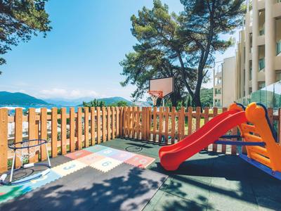 Kleiner Kinderspielplatz mit roter Rutsche neben einem Hotelgebäude und Blick auf Berge.