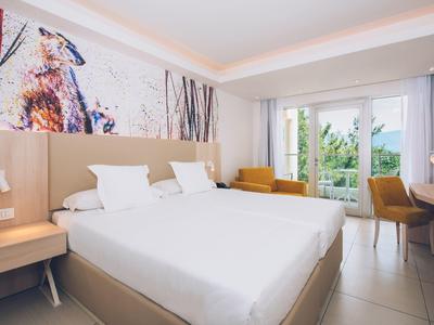 Modernes Hotelzimmer mit zwei Betten, Schreibtisch und Balkon mit Blick ins Grüne.