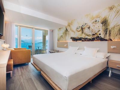 Nowoczesny pokój hotelowy z podwójnym łóżkiem, balkonem i widokiem na morze, jasny i przytulny.