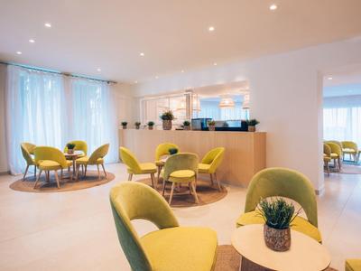 Nowoczesny salon hotelowy z żółtymi krzesłami, okrągłymi stolikami i miękkim oświetleniem.