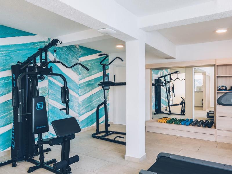 Siłownia z urządzeniami do ćwiczeń, jasne ściany i duże lustro.