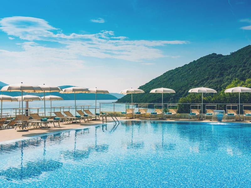 Luksusowy hotel z basenem na wybrzeżu w malowniczej zatoce z górami w tle.