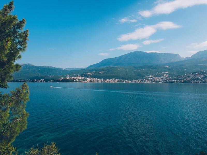 Widok na spokojne jezioro z górami i domami na brzegu pod niebieskim niebem.