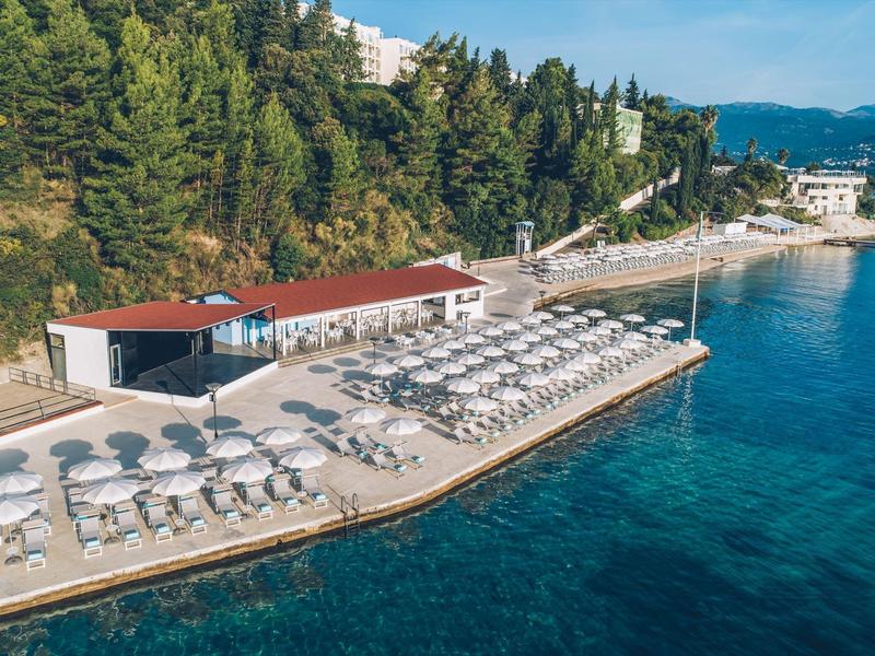 Nadmorska promenada z leżakami i parasolami obok czystej wody i zalesionego wzgórza.