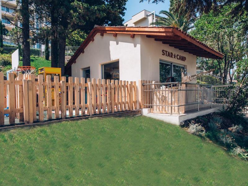 Mały budynek stacji z ogrodzonym terenem i trawiastym wzgórzem z przodu.