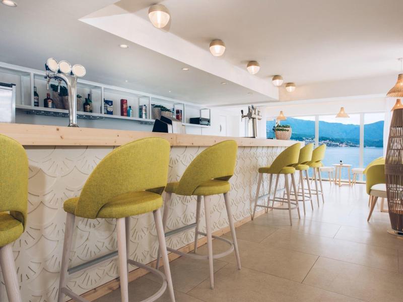 Nowoczesny bar z limonkowymi stołkami i widokiem na ocean przez duże okna.