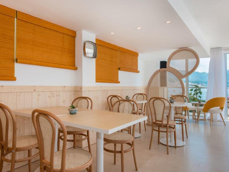 Jasna jadalnia hotelowa z drewnianymi krzesłami, białymi stołami i dużymi oknami z widokiem na góry.