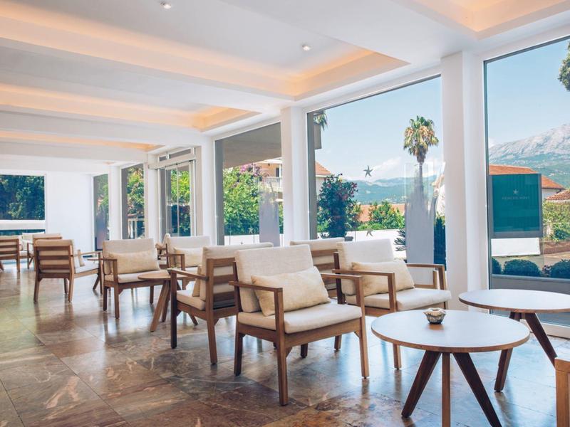 Przestronny hotelowy salon z naturalnym światłem, drewnianymi meblami i widokiem na palmy i ocean.