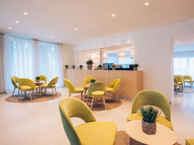 Nowoczesny salon hotelowy z żółtymi krzesłami, okrągłymi stolikami i miękkim oświetleniem.