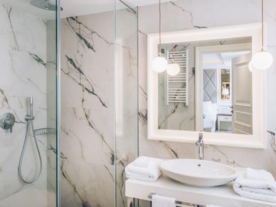 Bright bathroom with marble walls, large mirror, and modern shower.