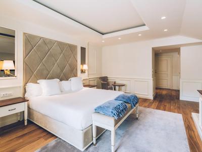 Modern hotel room with large double bed, table, chair, and wooden floor.